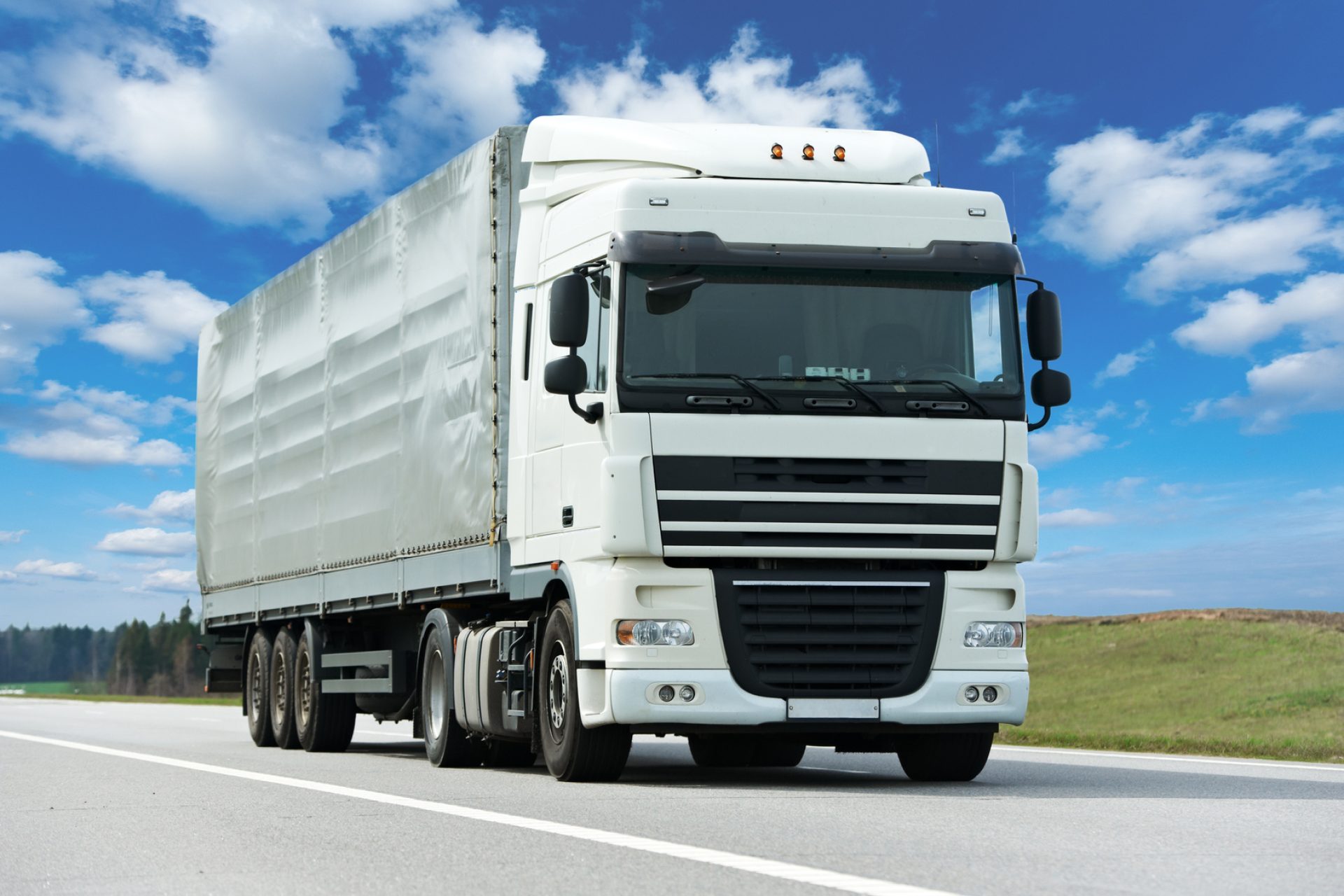 White lorry truck with grey trailer over blue sky on the road